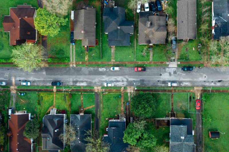High-angle aerial shot of a suburban neighborhood street lined with houses and cars